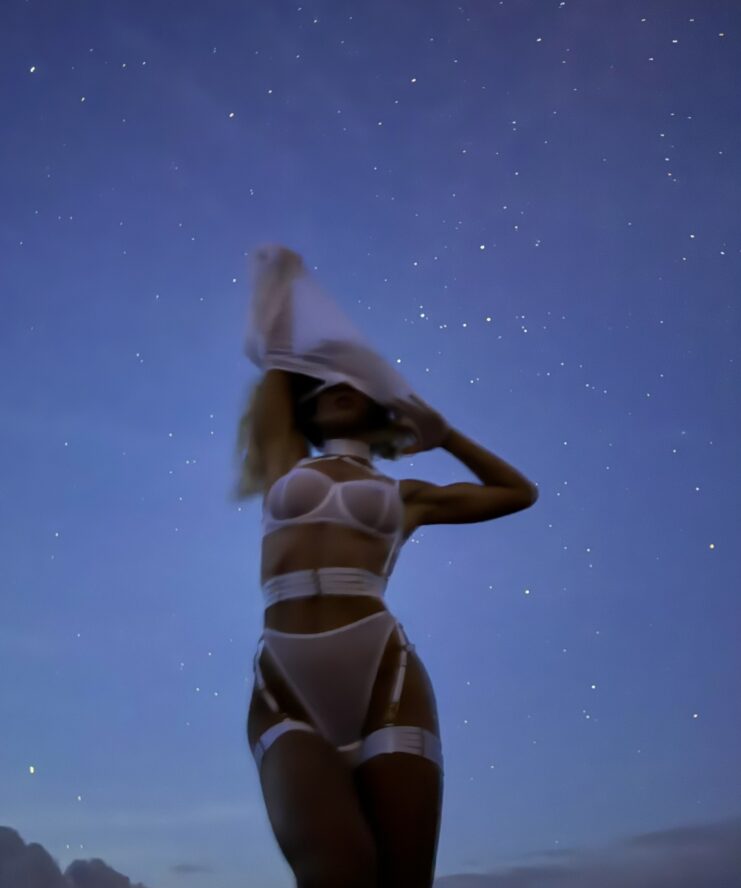 Night photography of woman stargazing wearing white lingerie and taking off her dress
